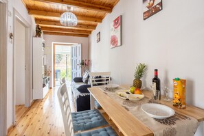 Enjoy a meal in the dining area with a long table set for two, featuring fresh fruit and a bottle of wine.