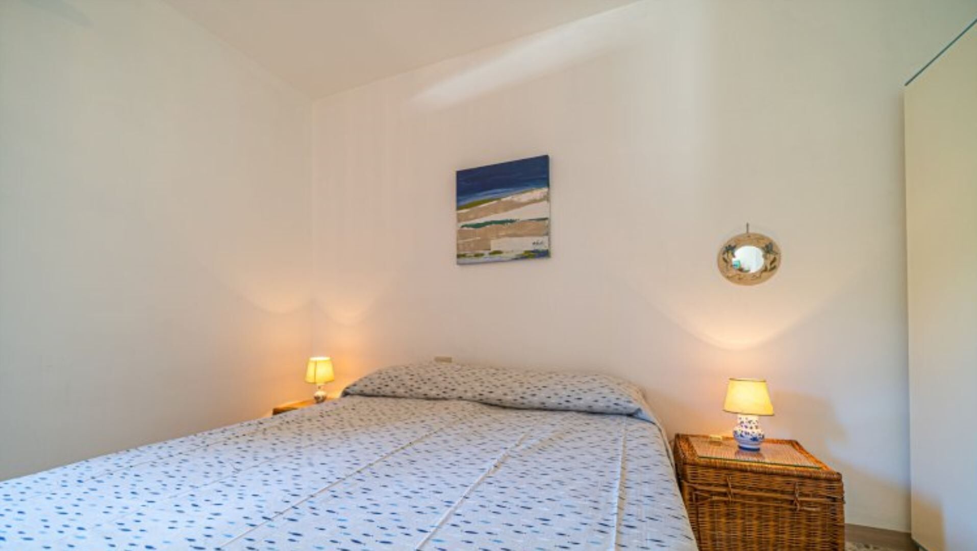 Une chambre à coucher avec un lit, deux lampes de chevet, un tableau accroché au mur et un petit panier en osier.
