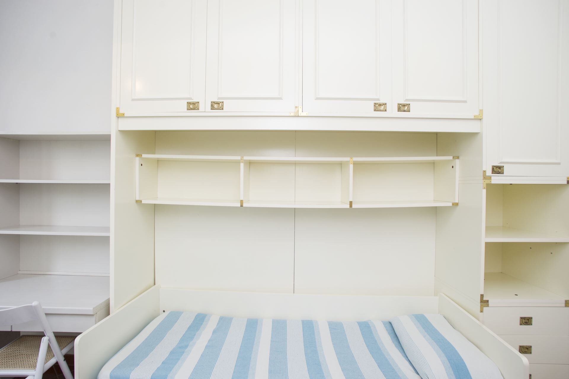 Ein heller Raum mit einem Bett, einem Sessel und einer Kommode mit Schubladen.