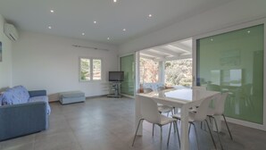 A spacious living area with a dining table and chairs, a sofa, a television, and a sliding glass door leading to a balcony.