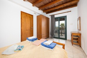 Een slaapkamer met een bed, een houten garderobe, een kleine tafel en een schuifdeur van glas die leidt naar een buitenruimte.
