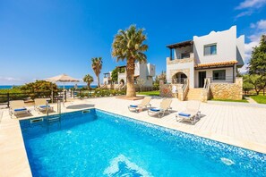 Uitzicht op een zwembad bij een moderne villa, met helderblauw water, ligbedden en een uitzicht op zee.
