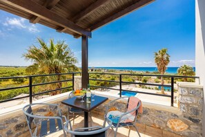 Een balkon met een tafel, stoelen, een fles en een schaal fruit.