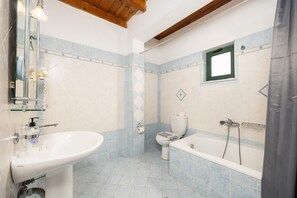 Een badkamer met een wastafel, toilet en bad, met blauw-witte tegels en een houten balk.