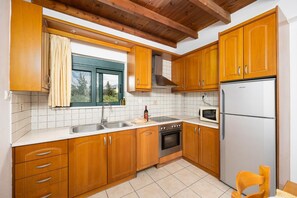 Eine Küche mit Holzausstattung, einem Edelstahlkühlschrank, einer Mikrowelle, einem Spülbecken und einem Fenster mit Vorhängen.
