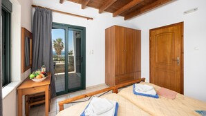 Une chambre comprenant un lit, une armoire en bois, un bureau avec un panier de fruits et une porte-fenêtre coulissante donnant sur un balcon.