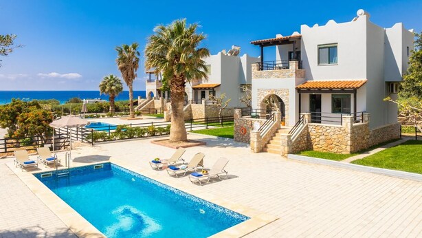 Un complexe hôtelier doté d’une piscine, de chaises longues, de palmiers et offrant une vue sur la mer.