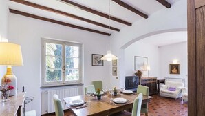Ein Essbereich mit einem Holztisch, gedeckt für vier Personen, einem Fenster mit Blick auf Grünflächen und einem Fernseher im Hintergrund.