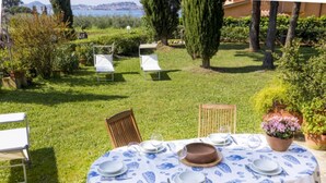 Ein Essbereich im Freien mit einem Tisch für vier Personen, umgeben von Stühlen, in einem üppigen Garten mit Meerblick.