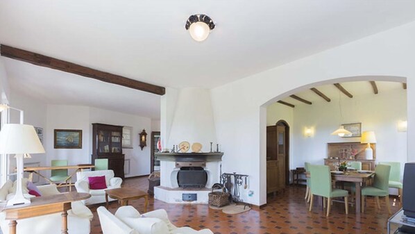A spacious living room with a fireplace, a dining area with green chairs, and a kitchen visible through an archway.