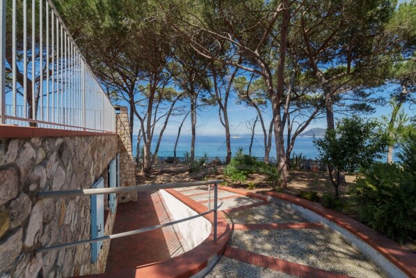 A stone building with a metal railing overlooking a coastal area with trees and a view of the sea.