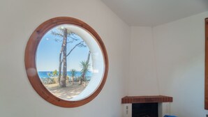 Una habitación con ventanal redondo que da a una playa, chimenea y sofá azul.