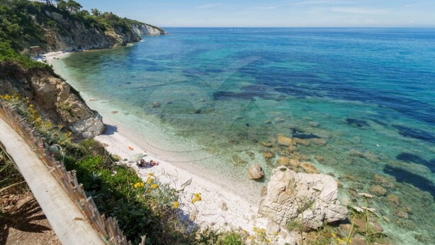 Una playa costera con agua cristalina, costa rocosa y una valla de madera.