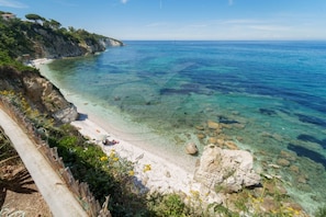 A coastal beach with clear water, rocky shore, and a wooden fence.