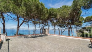 Un espacio exterior pavimentado con un muro de piedra y barandilla metálica, con vista a un cuerpo de agua.