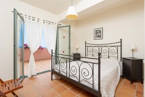 Une chambre à coucher comprenant un lit, une table de chevet, une chaise, une armoire et un balcon avec vue.