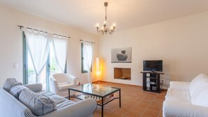 Un salon comprenant un canapé, un fauteuil, un téléviseur, une cheminée et un lustre.