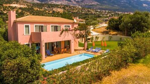 Une villa rose dotée d’une piscine, d’un espace salon extérieur et offrant une vue sur les montagnes.