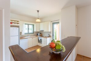 Une cuisine moderne avec des meubles blancs, un îlot central et un panier de fruits.