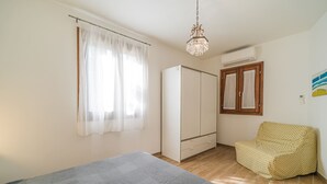 A bedroom with a bed, a wardrobe, a chair, a window with curtains, and a chandelier. - Casa al Mare in a panoramic position on the Gulf of Pareti (Capoliveri)