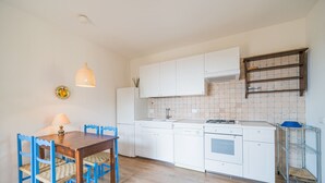 A compact kitchen with white cabinets, a wooden dining table with blue chairs, a hanging pendant light, and a tiled backsplash. - Casa al Mare in a panoramic position on the Gulf of Pareti (Capoliveri)