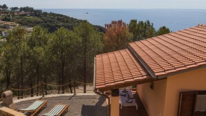 A terrace with a tiled roof overlooking a coastal landscape, featuring two lounge chairs and a dining table set for two. - Casa al Mare in a panoramic position on the Gulf of Pareti (Capoliveri)