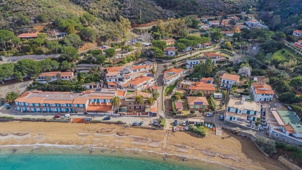 An aerial view of a coastal town with terraced houses, a beach, and clear turquoise waters. - Casa al Mare in a panoramic position on the Gulf of Pareti (Capoliveri)
