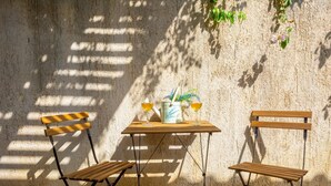 Una mesa con dos sillas, una botella y una copa de vino frente a una pared con textura.