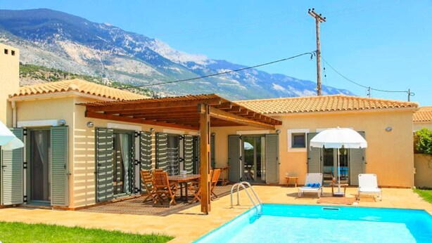 Zona de piscina con pérgola, mobiliario exterior y vistas a montañas.