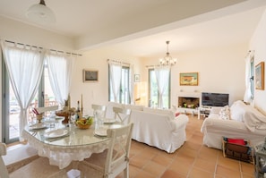 A spacious living area with a dining table set for four, a sofa, a TV, and a fireplace.