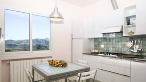 Et moderne køkken med hvide skabe, et glasbord med blomsterarrangement og udsigt til bjerge gennem vinduet.
