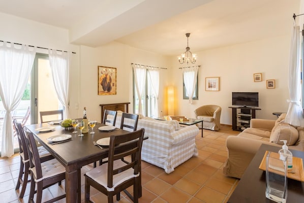 A dining area with a table set for four, a sofa, a TV, and a chandelier.