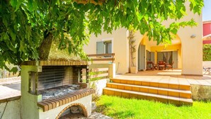 A patio area with a built-in grill, steps leading to a covered seating area, and a view of a building with shutters. - Villa Katerina - Three Bedroom Villa, Sleeps 6 (Afrato)