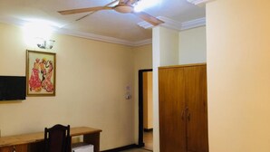 Ein Zimmer mit Deckenventilator, Schreibtisch mit Stuhl, kleinem Kühlschrank und Kleiderschrank.