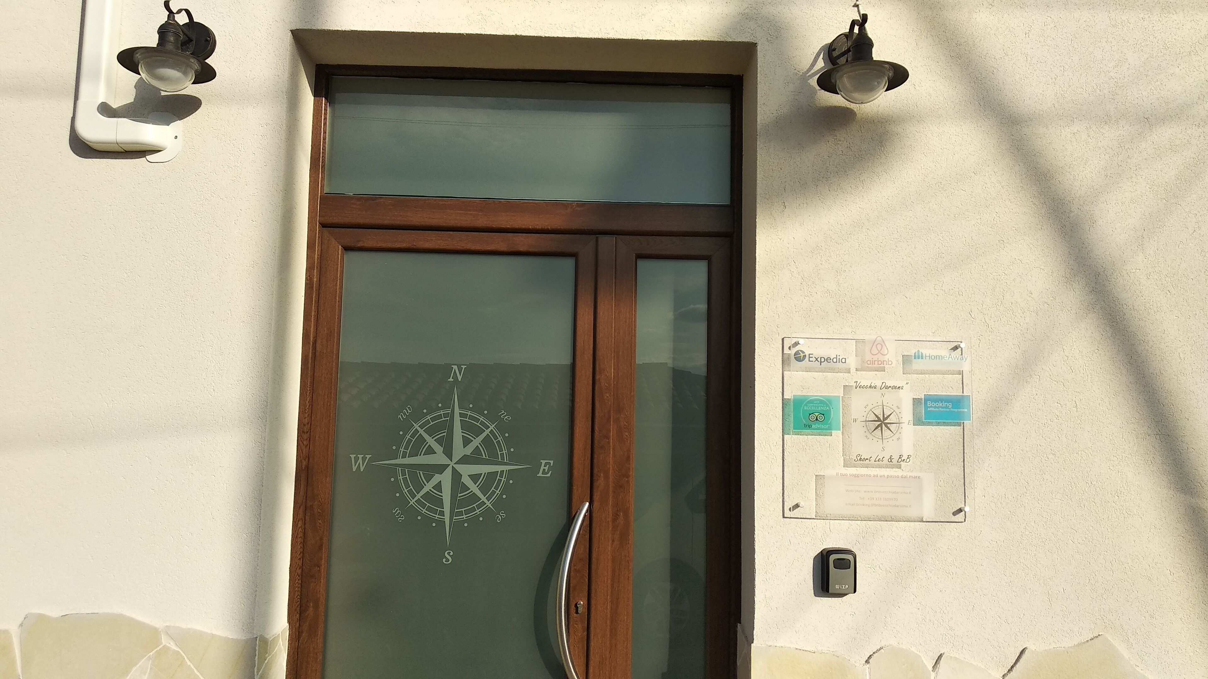 Une porte en bois ornée d’un motif de boussole, un panneau mural affichant des logos liés au voyage, et un dispositif de sécurité.