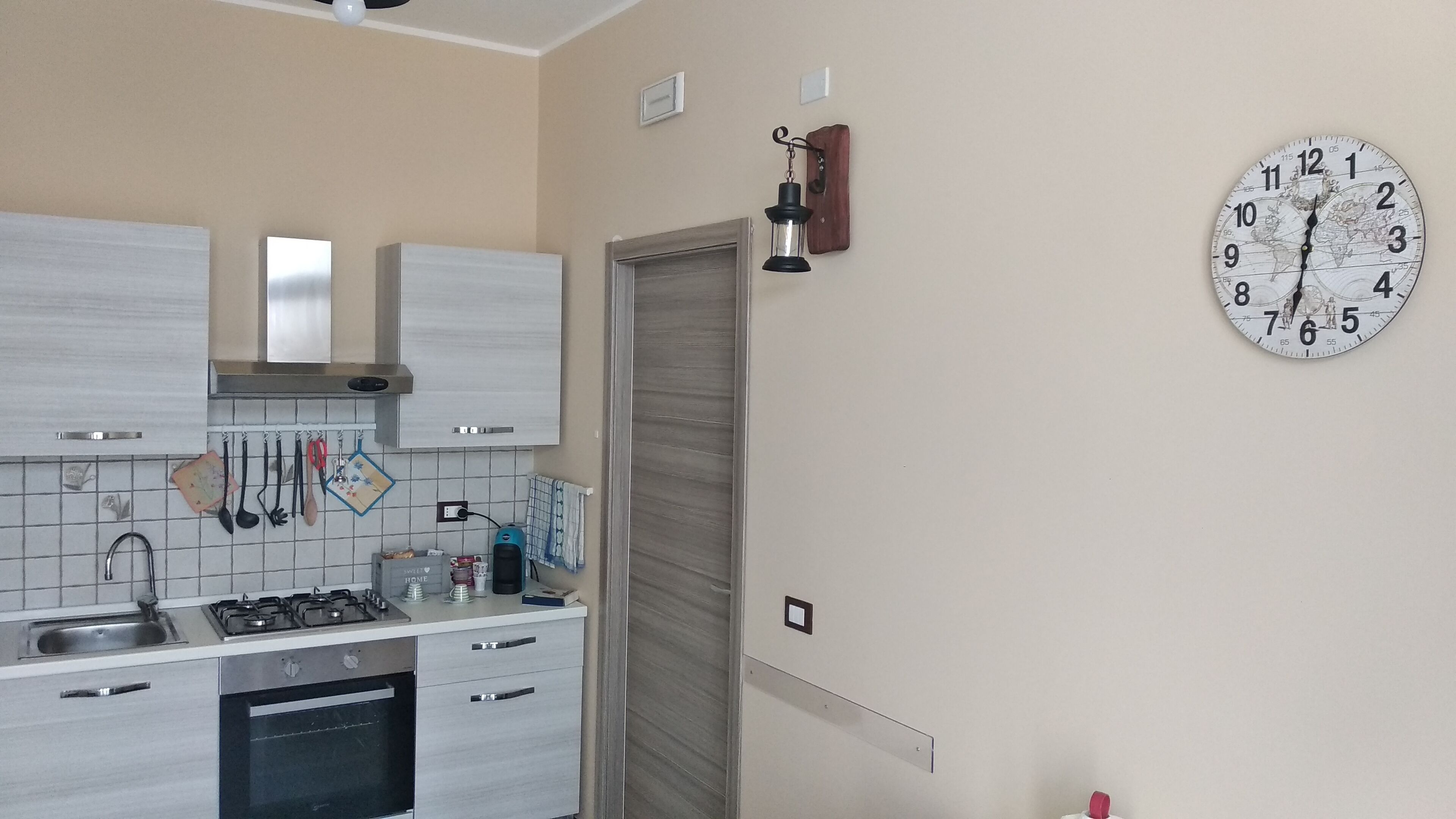 A kitchen with a gas stove, oven, and cabinets. There is a clock on the wall and a door with a handle.