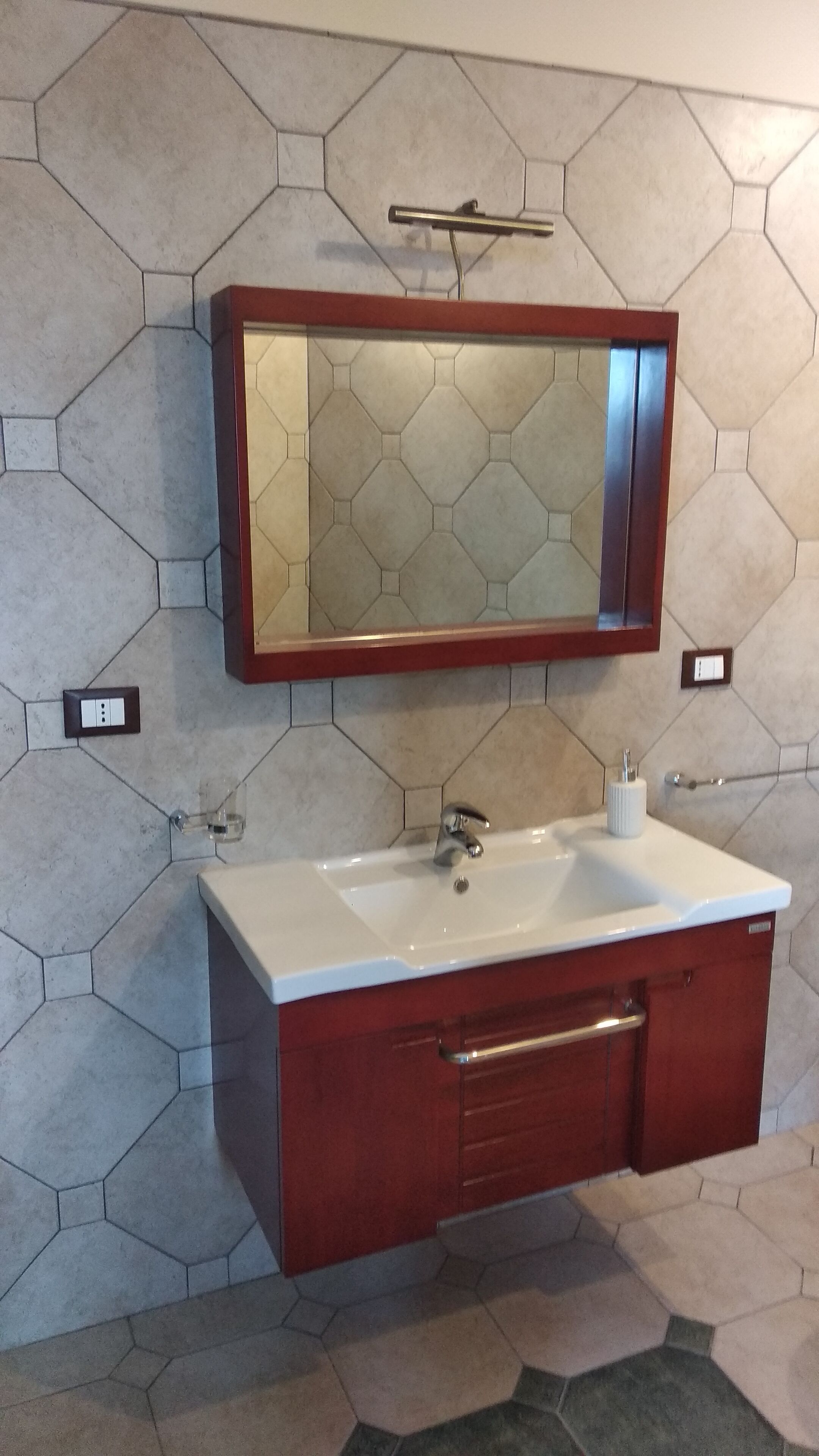A bathroom with a hexagonal tile backsplash, a white sink with a wooden vanity, and a mirror with a wooden frame.