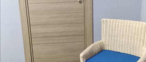 A room with a wooden door, a wicker chair with a blue cushion, and grey tiled flooring.