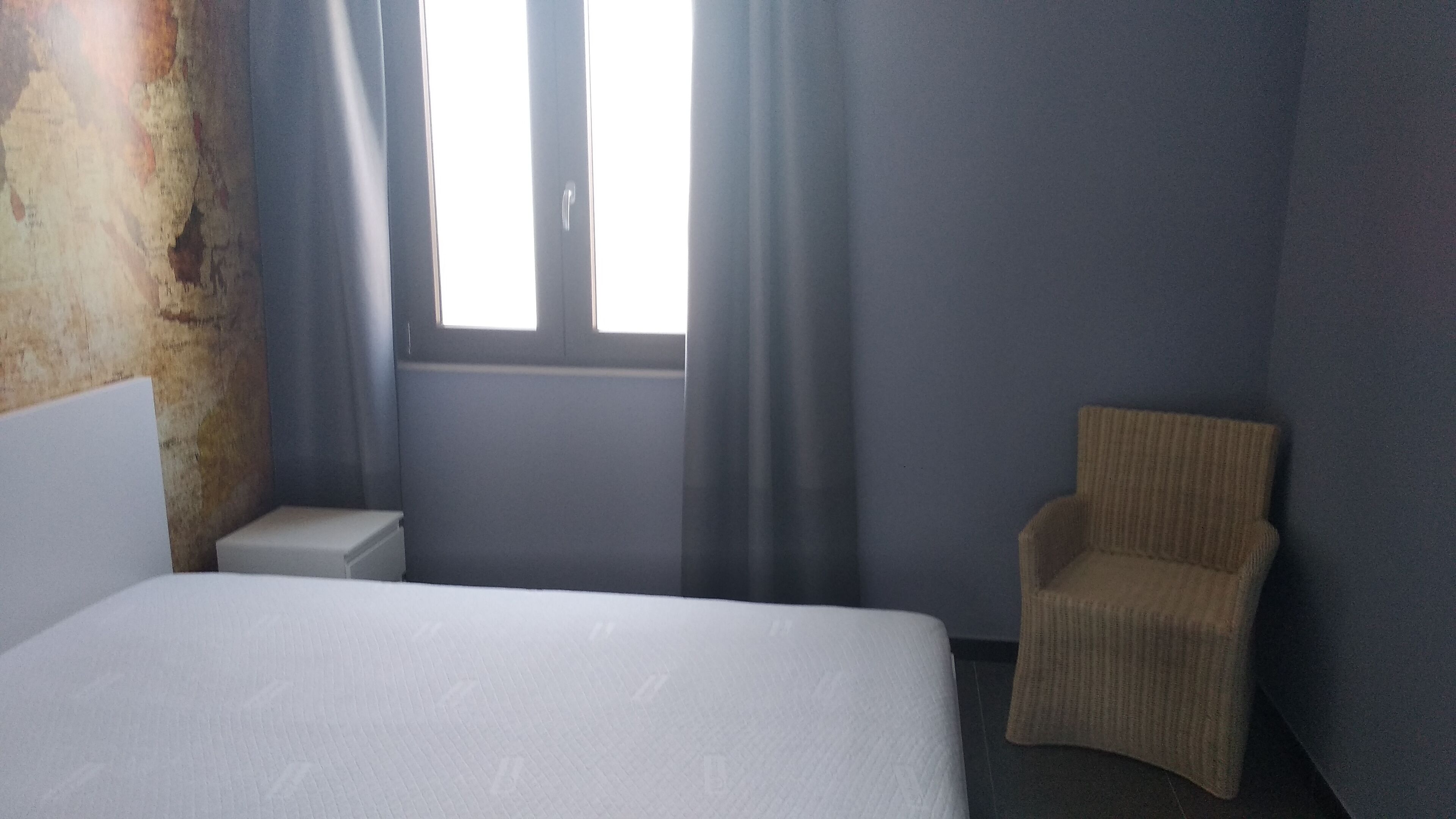 Una habitación de hotel con cama, una silla, una mesita de noche y una ventana con cortinas.