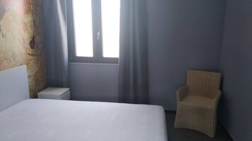 Una habitación de hotel con cama, una silla, una mesita de noche y una ventana con cortinas.