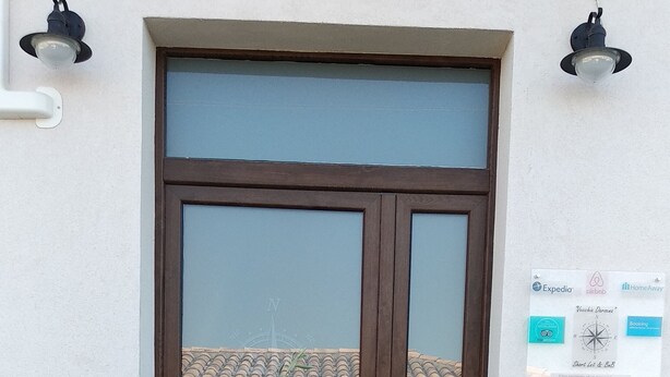 Una entrada de edificio con fachada de piedra, puerta de madera y planta en maceta con flores rosadas.