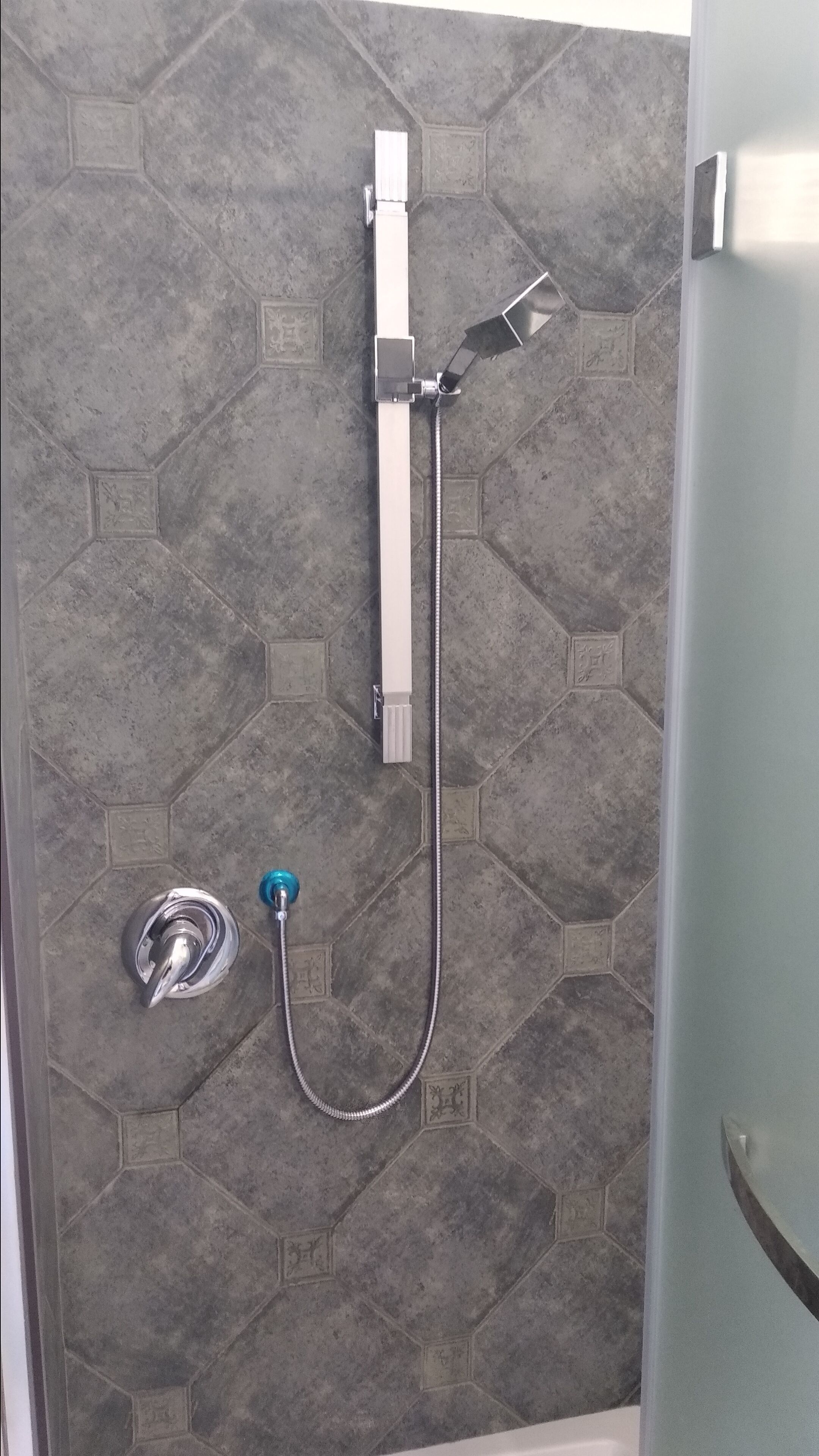 A shower with a handheld showerhead and a wall-mounted control panel.