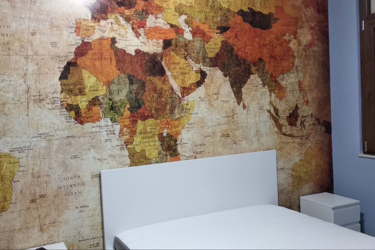 Eine Weltkarte an der Wand in einem Zimmer mit Bett und Nachttisch.