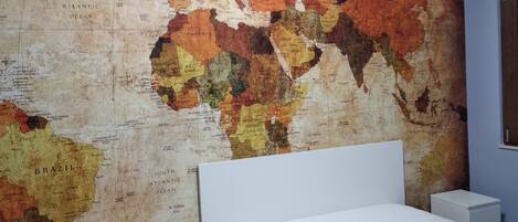 A world map on a wall in a room with a bed and a nightstand.
