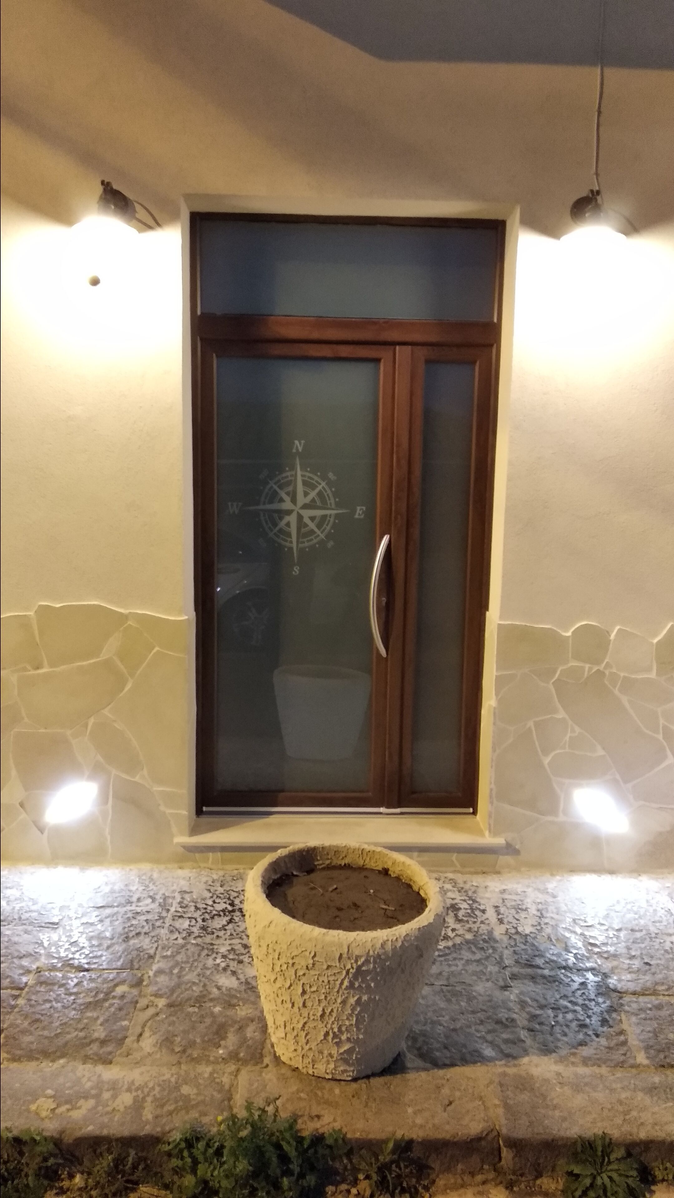 A door with a compass design, a stone planter in front, and a stone wall with a crack.