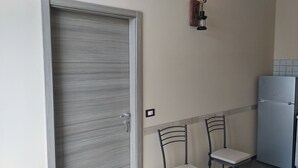 Una cocina con puerta de madera, un refrigerador y dos sillas.