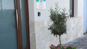 Un edificio de fachada de piedra, una maceta grande con flores rosadas y un letrero con una brújula.