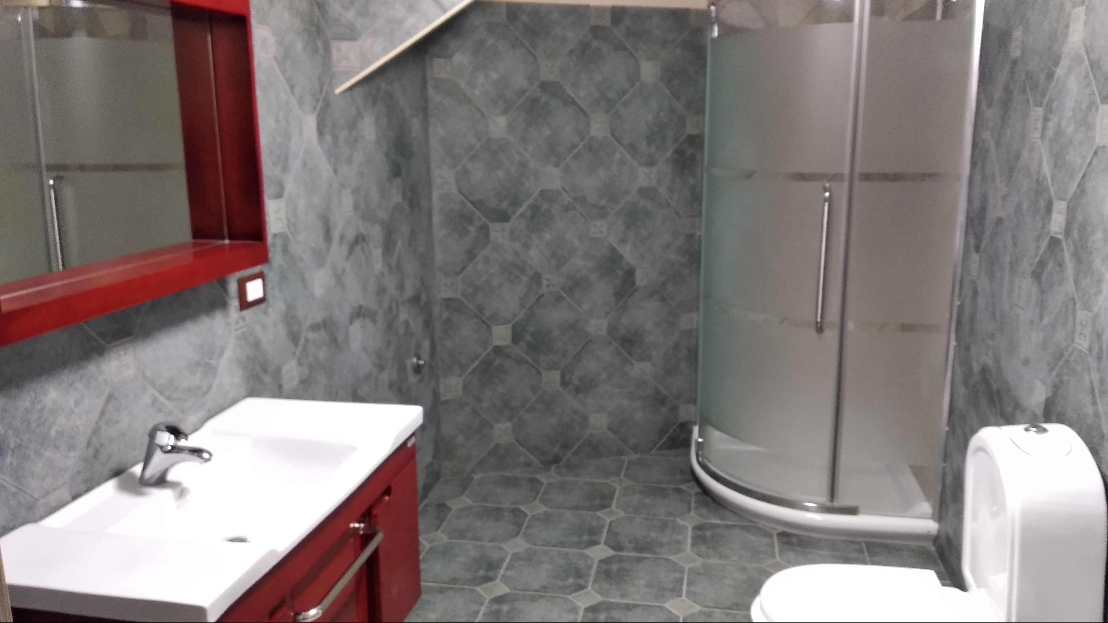 Une salle de bain avec un lavabo blanc, un meuble rouge et une cabine de douche en verre.