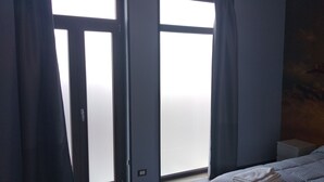 Una habitación con cama, mesita de noche y ventana con cortinas.