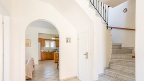 Un pasillo amplio con suelo de baldosas que conduce a una zona de cocina con armarios de madera y un comedor con una silla estampada de cebra.